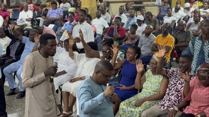 A congregation worshipping while a speaker holds a microphone