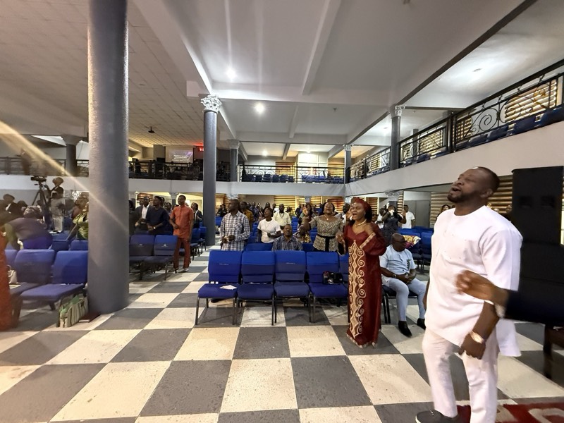 A man in white addressing people gathered in a hall