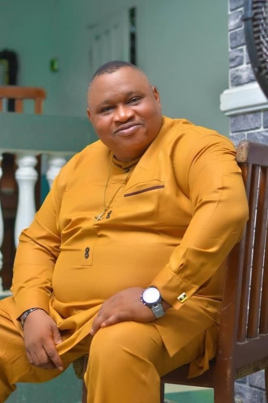 A minister seated, wearing orange attire
